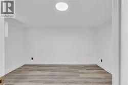Neutral white walls featuring wood-finish flooring, white baseboards, and a circular ceiling light fixture - 