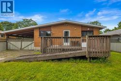 Rear exterior featuring a wood deck with an integrated ramp, brick facade, covered carport, and private yard space - 