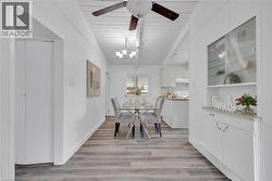Dining area featuring wood-finish flooring, white paneled walls, and a white ceiling with a dark-bladed ceiling fan - 
