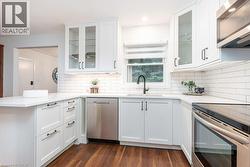 Modern kitchen featuring white shaker-style cabinetry, stainless steel appliances, white subway tile backsplash, and wood-finish flooring - 