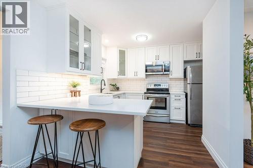 Modern kitchen featuring white cabinetry, subway tile backsplash, stainless steel appliances, wood-finish flooring, and a breakfast bar with white countertop - 139 Mackay Crescent, Waterloo, ON 