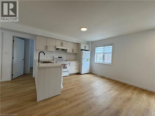 Open-concept kitchen and living area featuring wood-finish flooring, light-toned cabinetry, a central kitchen island with integrated sink, white appliances, and a window with horizontal blinds - 113 Highriver Trail Unit# Main, Welland, ON - Indoor Photo Showing Kitchen