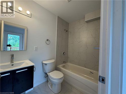 Bathroom featuring a vanity with a white basin and dark wood-finish cabinetry, a toilet, and a bathtub with white-veined tile surround - 113 Highriver Trail Unit# Main, Welland, ON - Indoor Photo Showing Bathroom