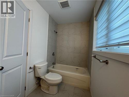 Bathroom featuring a white toilet, full-sized bathtub with shower, and tiled surround - 113 Highriver Trail Unit# Main, Welland, ON - Indoor Photo Showing Bathroom