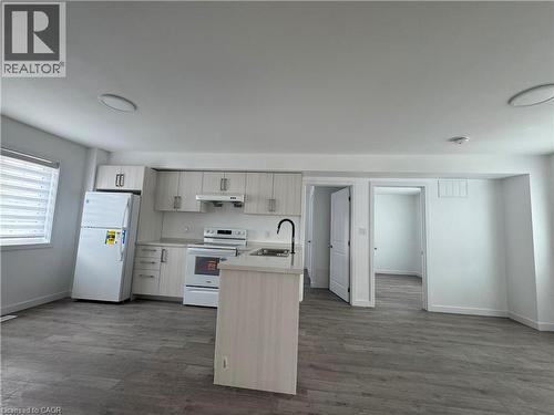 Open-concept kitchen featuring light-toned cabinetry, a central island with an integrated sink and gooseneck faucet, white appliances, and wood-finish flooring - 119 Highriver Trail Unit# Main, Welland, ON - Indoor Photo Showing Kitchen