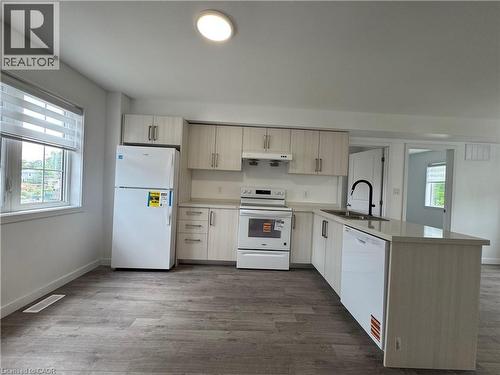 Kitchen featuring wood-finish cabinetry, white appliances, a center island with sink and integrated dishwasher, and wood-finish flooring - 119 Highriver Trail Unit# Main, Welland, ON - Indoor Photo Showing Kitchen With Double Sink