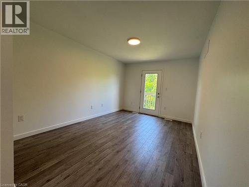 Spacious room featuring wood-finish flooring, white baseboards, and a rear door with a full-pane glass insert leading to an exterior balcony - 133 Highriver Trail Unit# Main, Welland, ON 