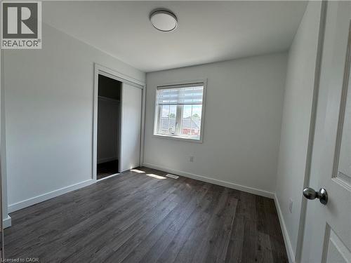 Room featuring wood-finish flooring, white baseboards, and a window with horizontal blinds - 133 Highriver Trail Unit# Main, Welland, ON 
