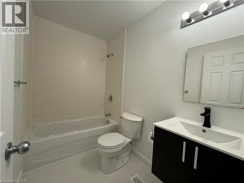 Bathroom featuring a white bathtub, subway tile surround, white toilet, dark wood-finish vanity with an integrated sink, and a matte black faucet - 133 Highriver Trail Unit# Main, Welland, ON 