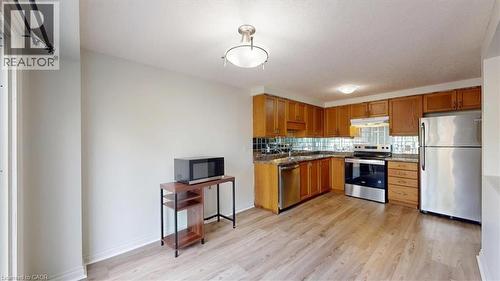 Kitchen featuring wood-finish flooring, warm-toned cabinetry, stainless steel appliances, and a tile backsplash - 980 Creekside Drive, Waterloo, ON - Indoor Photo Showing Kitchen With Stainless Steel Kitchen