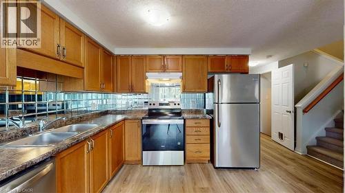 Kitchen featuring wood cabinetry, stainless steel appliances, a double basin sink, and a mirrored tile backsplash - 980 Creekside Drive, Waterloo, ON - Indoor Photo Showing Kitchen With Stainless Steel Kitchen With Double Sink