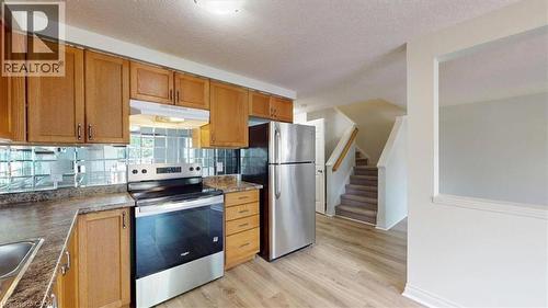 Kitchen featuring wood cabinetry, stainless steel appliances, a mirrored tile backsplash, and wood-finish flooring - 980 Creekside Drive, Waterloo, ON - Indoor Photo Showing Kitchen