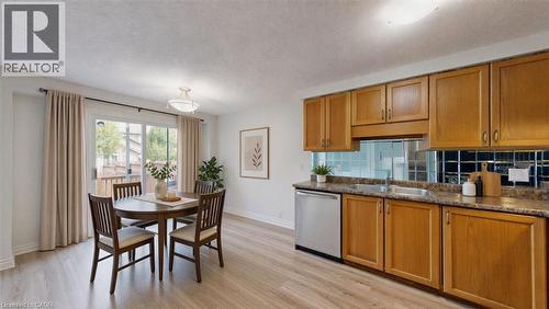 Kitchen and dining area featuring wood-finish flooring, light wood cabinetry, stone-finish countertops, stainless steel dishwasher, and a sliding glass door - Virtually staged - 980 Creekside Drive, Waterloo, ON - Indoor
