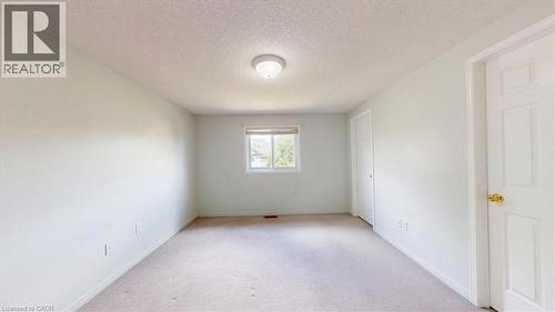 Neutral toned bedroom featuring light-colored carpet, a double-panel interior door with brass hardware, and a single window offering exterior light - 980 Creekside Drive, Waterloo, ON - Indoor Photo Showing Other Room