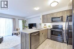 Open-concept kitchen featuring wood-finish cabinetry, stainless steel appliances, a center island with sink, and light-toned countertops - 