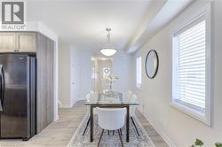 Bright dining area featuring light wood-finish flooring, two large windows with blinds, a ceiling-mounted light fixture, and a neutral wall color - 
