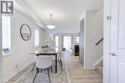 Open-concept dining area featuring light wood-finish flooring, a contemporary ceiling fixture, two windows with blinds, and white baseboards - 