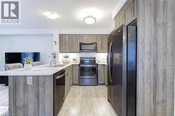 Kitchen featuring wood-finish cabinetry, light-toned countertops, and integrated black appliances - 