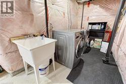 Laundry area featuring a utility sink with a dual-handle faucet, side-by-side laundry machines, and a storage shelf - 