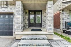 Stone facade with dual entry doors featuring decorative wrought iron inserts, an overhead porch light, and a paneled garage door - 