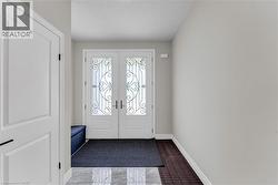 Entryway featuring double doors with decorative wrought iron detailing and frosted glass inserts, a white paneled interior door, light gray wall paint, and a combination of patterned tile and dark tex - 