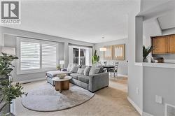 Open-concept living space featuring neutral carpet flooring, a large window with white plantation shutters, and a sliding glass door - 