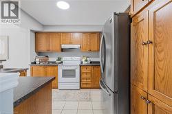 Kitchen featuring wood cabinetry, dark speckled countertops, tile flooring, stainless steel refrigerator, and white range with matching hood vent - 