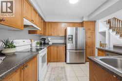 Kitchen featuring wood cabinetry, dark speckled countertops, white appliances, a stainless steel refrigerator, and tiled flooring - 