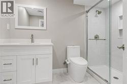 Bathroom featuring a single-sink vanity with white cabinetry and a white countertop, a frameless shower with a glass enclosure and a built-in shower niche, and a modern toilet - 