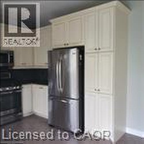 Kitchen featuring white shaker-style cabinetry, dark countertops, a built-in microwave, and a stainless steel refrigerator - 249 Bussel Crescent, Milton, ON 