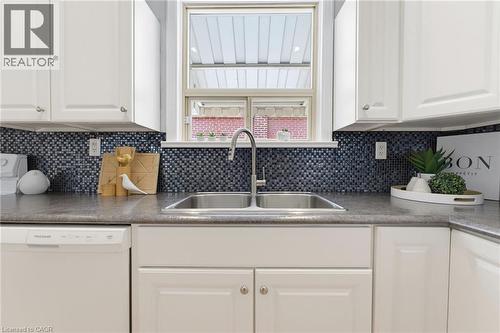 Kitchen workspace featuring white cabinetry, a double basin stainless steel sink with a gooseneck faucet, a dark mosaic tile backsplash, and a built-in dishwasher - 282 East 13Th Street, Hamilton, ON - Indoor Photo Showing Kitchen With Double Sink