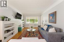 Spacious living area featuring wood-finish flooring, a white stone-finish fireplace, and built-in shelving - 