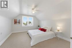 Attic room featuring a single window with blinds, sloped ceilings, and light-toned carpeting - 