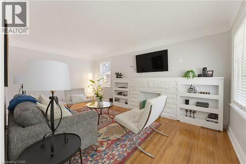 Living area featuring wood-finish flooring, a white stone-clad fireplace surround, built-in shelving, crown molding, and natural light - 282 East 13Th Street, Hamilton, ON 