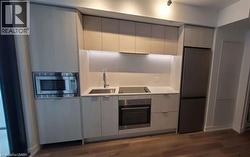 Modern kitchen featuring integrated appliances, under-cabinet lighting, a built-in microwave, and wood-finish flooring - 