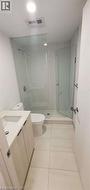 Modern bathroom featuring a glass-enclosed shower with white mosaic tile, a white toilet, a vanity with a white countertop and integrated sink, and light-toned cabinetry - 