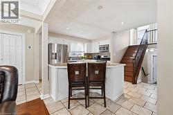 Kitchen featuring an island with seating, stainless steel appliances, tile flooring, white cabinetry, and a subway tile backsplash - 