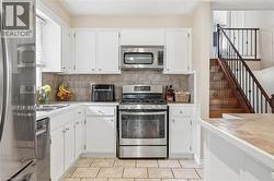 Kitchen featuring white cabinetry, stainless steel appliances, a tiled backsplash, and light-toned floor tiles - 