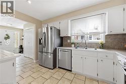 Kitchen featuring white cabinetry, stainless steel refrigerator and dishwasher, a double basin sink, and tile flooring - 
