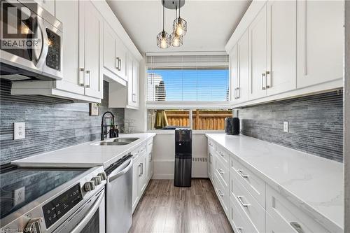 Galley kitchen featuring white shaker cabinetry, stainless steel appliances, a tile backsplash, light-toned countertops, and wood-finish flooring - 15 Nicklaus Drive Unit# 17, Hamilton, ON 