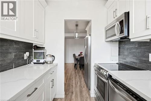 Galley kitchen featuring white cabinetry, light-toned countertops, and a dark horizontal tile backsplash - 15 Nicklaus Drive Unit# 17, Hamilton, ON 