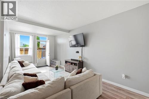 Spacious living area featuring light-toned walls, wood-finish flooring, and a large window providing outdoor access - 15 Nicklaus Drive Unit# 17, Hamilton, ON 