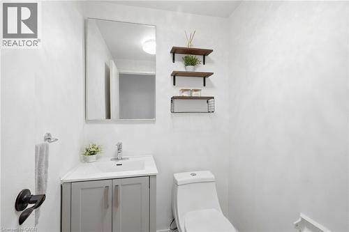 Compact bathroom featuring a corner vanity with a white countertop and gray cabinetry, a wall-mounted mirror, a two-piece toilet, and three wall-mounted shelves - 15 Nicklaus Drive Unit# 17, Hamilton, ON 