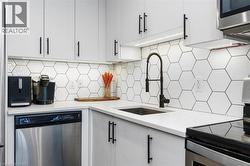Modern kitchen featuring white cabinetry with matte black hardware, hexagonal tile backsplash, white countertops, and stainless steel appliances - 