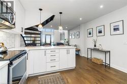 Contemporary kitchen featuring white cabinetry, stainless steel appliances, a white hexagonal tile backsplash, and dark wood-finish flooring - 