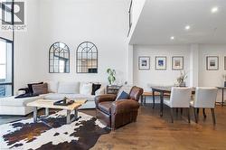 Open-concept living area featuring high ceilings, tall windows with dark framing, wood-finish flooring, and recessed lighting - 