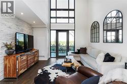 Two-story floor-to-ceiling windows with dark frames, a white stacked stone accent wall, recessed lighting, and dark wood-finish flooring - 