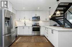 Contemporary kitchen featuring white cabinetry with black hardware, stainless steel appliances, hexagon tile backsplash, and wood-finish flooring - 