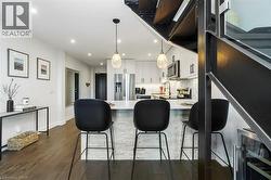 Modern kitchen and dining area featuring dark wood-finish flooring, white cabinetry with matte black hardware, stainless steel appliances, and a hexagon tile backsplash - 
