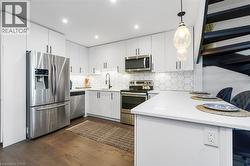 Modern kitchen featuring white cabinetry, stainless steel appliances, hexagon tile backsplash, and an eat-at peninsula with pendant lighting - 